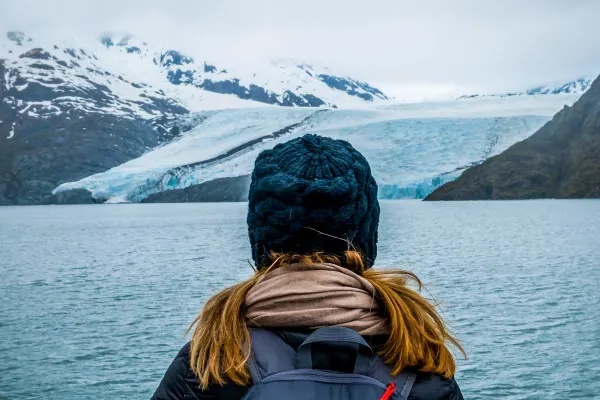 Behind shot of a woman wearing a beanie looking out at ice and snow-covered mountains from a cruise ship