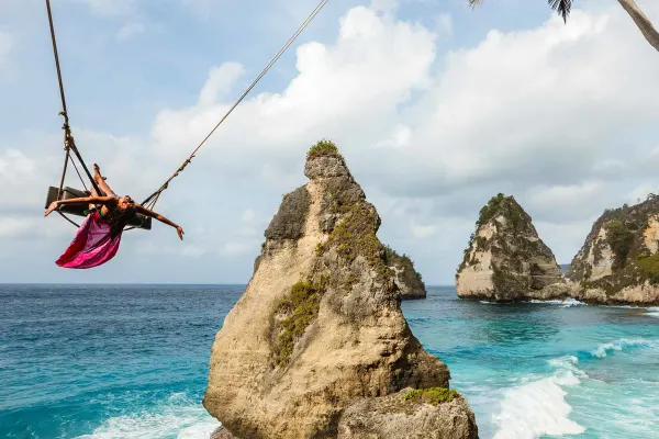 Woman on a large swing, above crashing waves