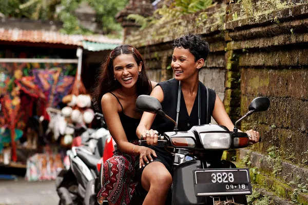 Happy female friends enjoying scooter ride in alley during vacation
