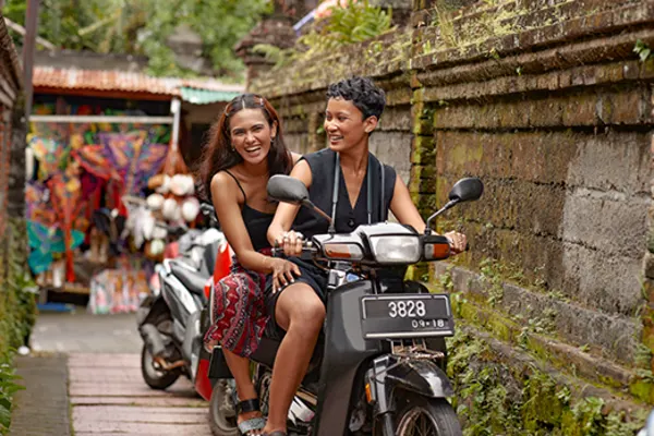 two people on a motorbike riding down small street in bali