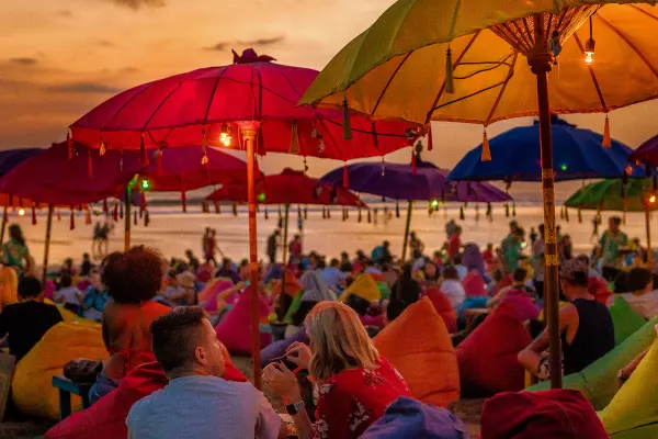 ourists relaxing and sitting on colorful bean bags, under the umbrellas, and enjoying the sunset at the beach