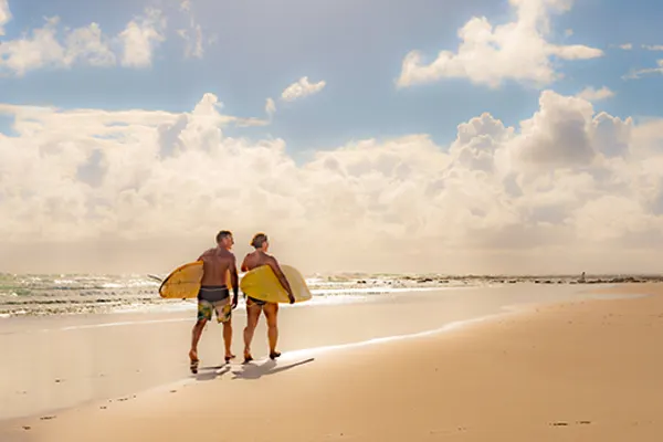 Walking along beach holding surf boards