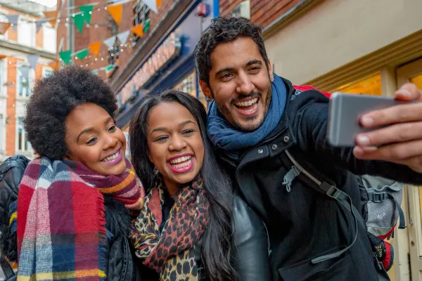 Three people smiling taking a selfie in a street lined with orange, green and white flags