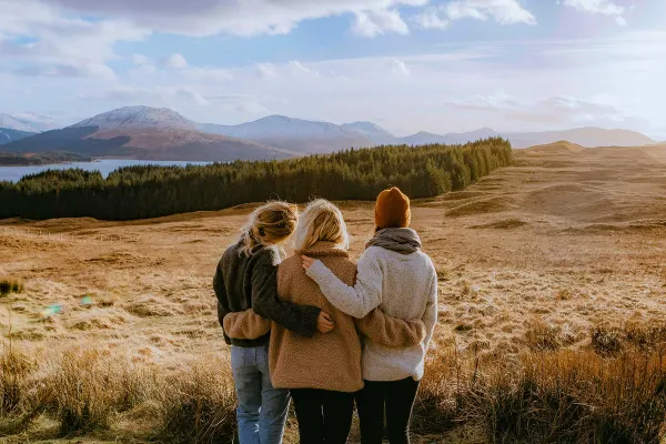 Three women arm in arm watching a sunset on a tall, grassy plain