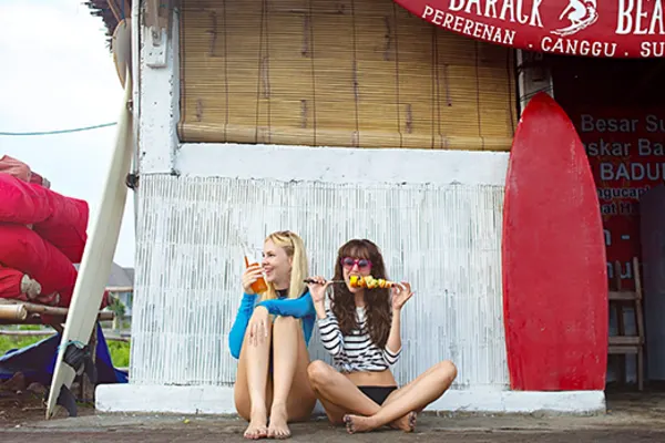 two girls sitting on ground outide of shop eating in canggu