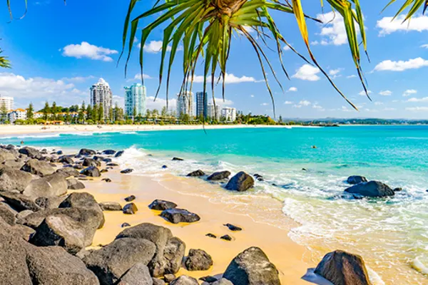 Vibrant shot of rocks on a beach with the city of Coolangatta in the background