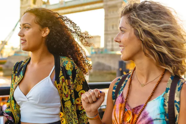 Two women posing in front of Tower Bridge in London at sunset