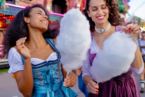 Two people in fancy dresses eating cotton candy at a theme park