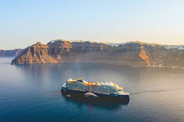Wide shot of a cruise ship sailing past steep rocky cliffs