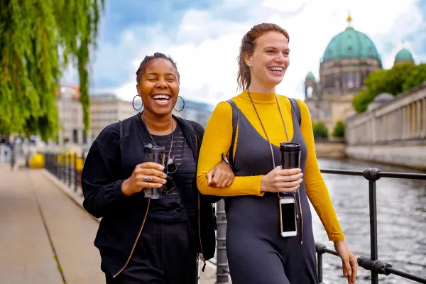 Cheerful friends walking on footpath by river in city