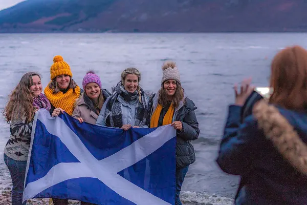 Group of friends next to loch holding Scottish flag