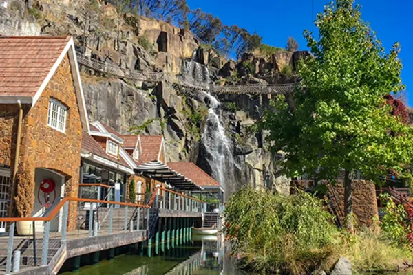 Line of buildings along a rocky cliff with a waterfall in the background