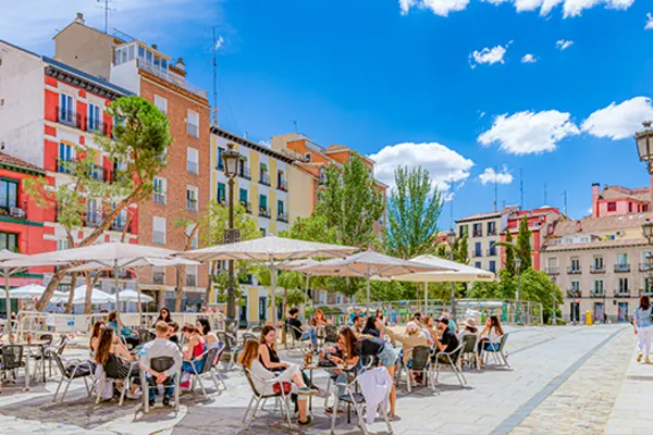 Dozens of people sitting having lunch under umbrellas in a city square in Madrid