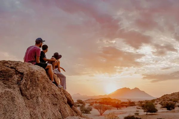 Three people sitting on rocks watching a sunset over the plains in Africa