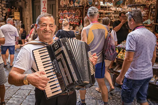Man smiling, playing the accordion in a busy shopping street
