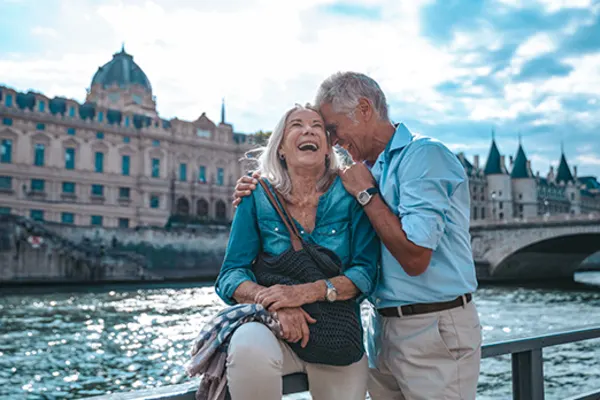 old couple standing by river in paris laughing