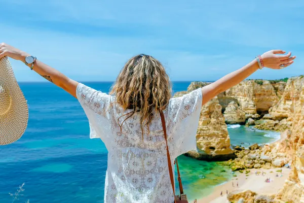 Woman with arms spread looking out over the ocean from a high cliff