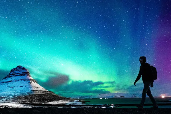 Night time shot of someone walking along beneath the Northern Lights