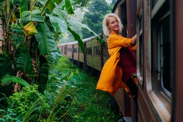 Woman on the edge of a train going through a lush rainforest