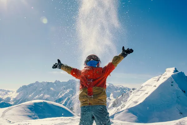 Snowboarder throwing powder into the air on a snow field on a sunny day
