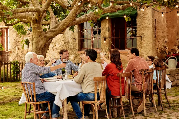 People eating at a long wooden table outside under a tree covered in hanging lights