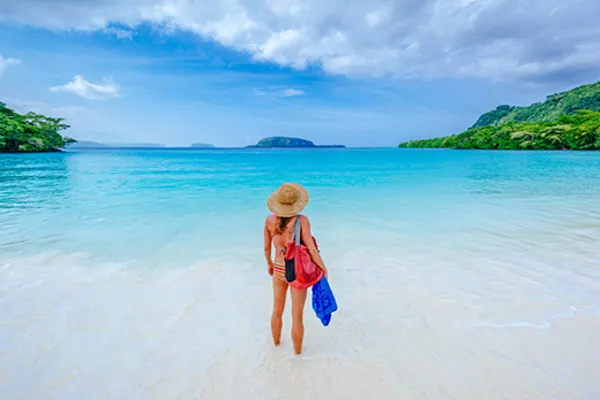 Women standing in shallow ocean water, looking out at tropical islands