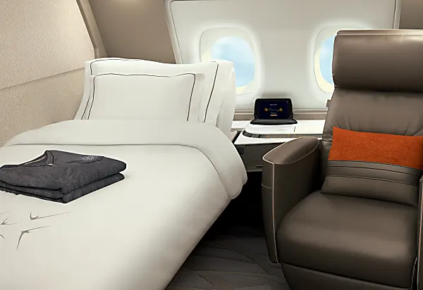 Singapore Airlines first class suite featuring single bed with white sheets and a reclining spacious seat with two windows.