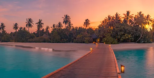 Board walk in the Maldives set over the water with a sunset over the palms