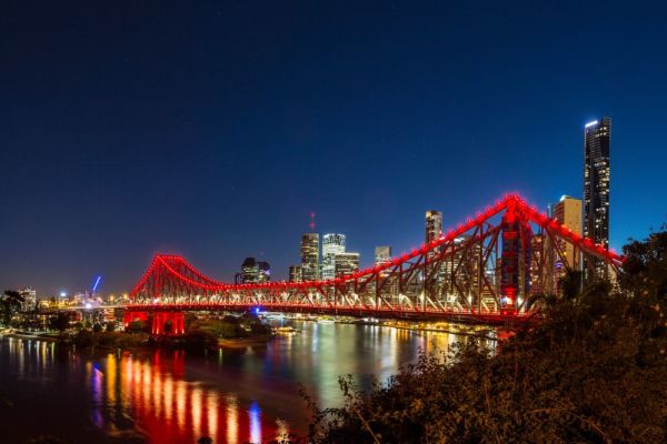 Brisbane cross the river bridge lite up red with city view in background during nighttime