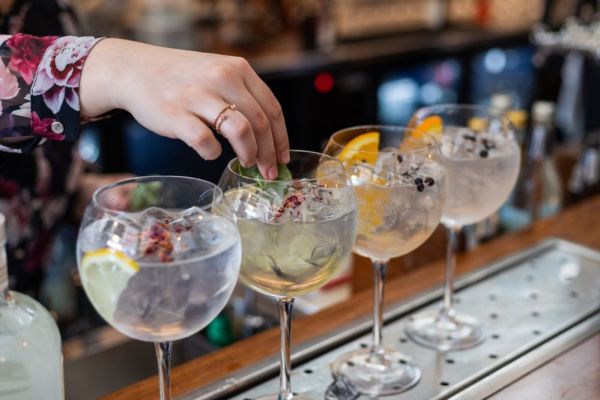 4 cocktail drinks being made on a bar top, bar staff placing berries in glasses