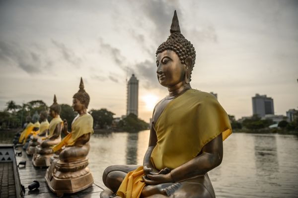 Row of statue Buddhist sat on a bridge overlooking a lake and temple