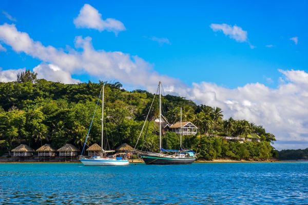 Boats sailing through ocean passing some huts in Vanuatu