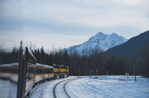 Train travelling along a snow-covered railroad with mountains in the background.