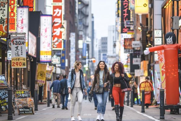 Group of females walking through a street with lite up signs in Tokyo