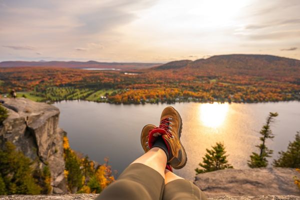 Hiker legs hanging over mountain ledge looking at river during sunset