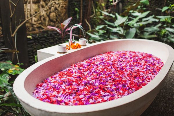 Stone bathtub filled with water, pink and purple flower petals lay on top