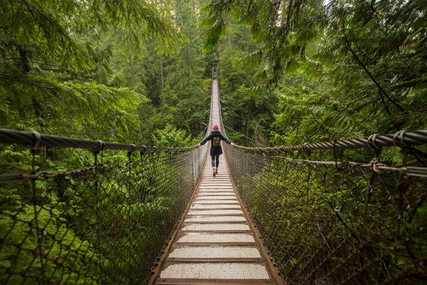 Hiker walking across wooden suspension bridge in middle of the forest