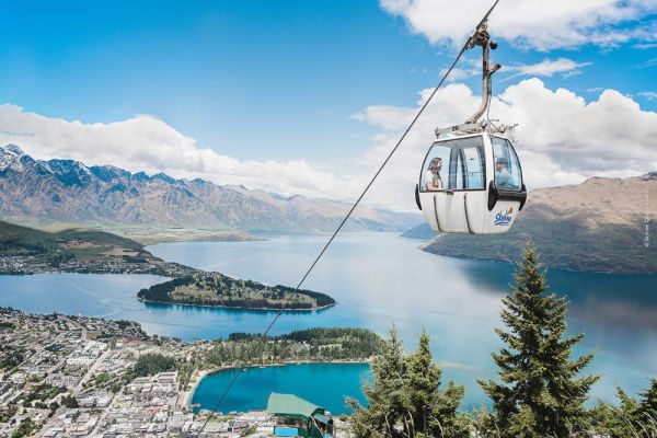 People going up in the Gondola with town of Queenstown and ocean views are in the background