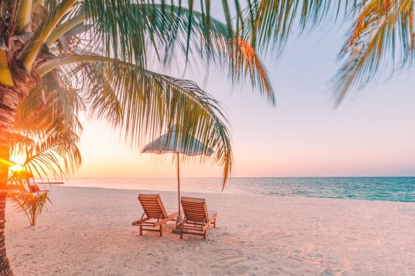 Two beach chairs and umbrella on beach front during sunrise
