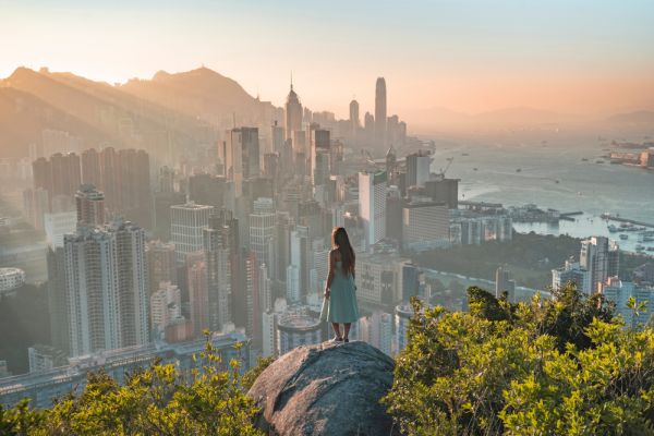 Woman standing on edge of a mountain on a rock looking at Hong Kong city as the sun sets