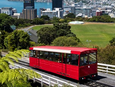Single cart red train on track with CBD of Wellington is in the background