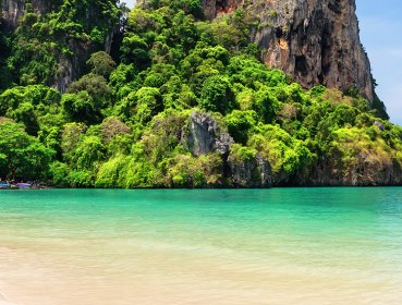 Wide angle shot of canoe half on shore half in water on an island beach located in Phuket