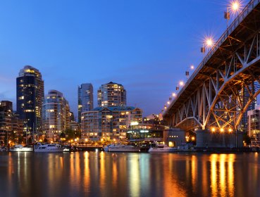 City view under Vancouver bridge with lights reflecting off river water during dusk