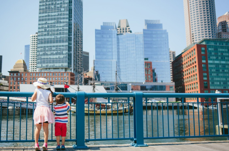 kids holding onto an iron fence, looking at the Boston city skyline