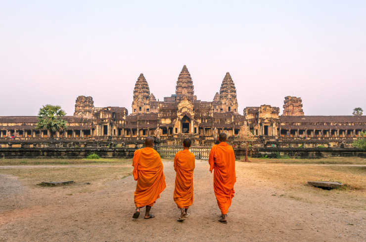 Three Buddhist monks in orange robes standing in front of Angkor Wat