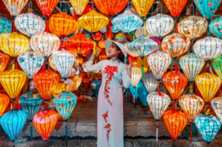 lady wearing traditional vietnamese clothing standing in front of a wall of lanterns