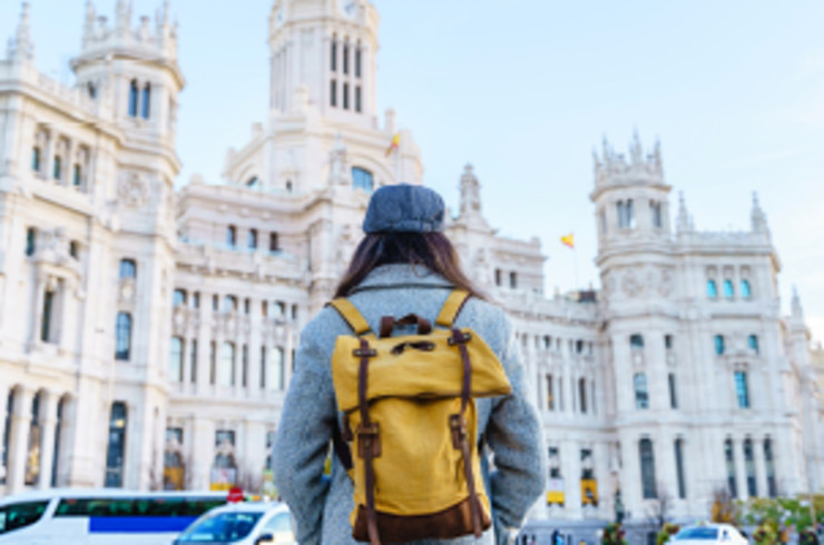 traveller with yellow backpack looking up at large white madrid building
