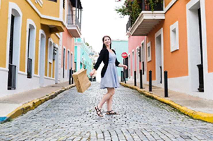 lady swinging bag and walking happily down a street lined by colourful buildings in san juan