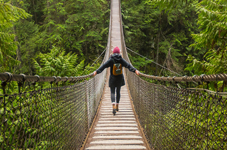 lady walking across suspension bridge surrounded by forest