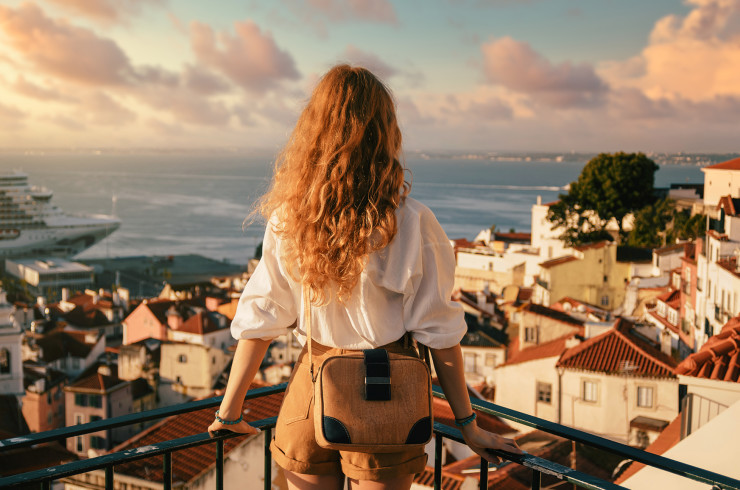 Woman with curly brown hair at a balcony looking over a seaside town